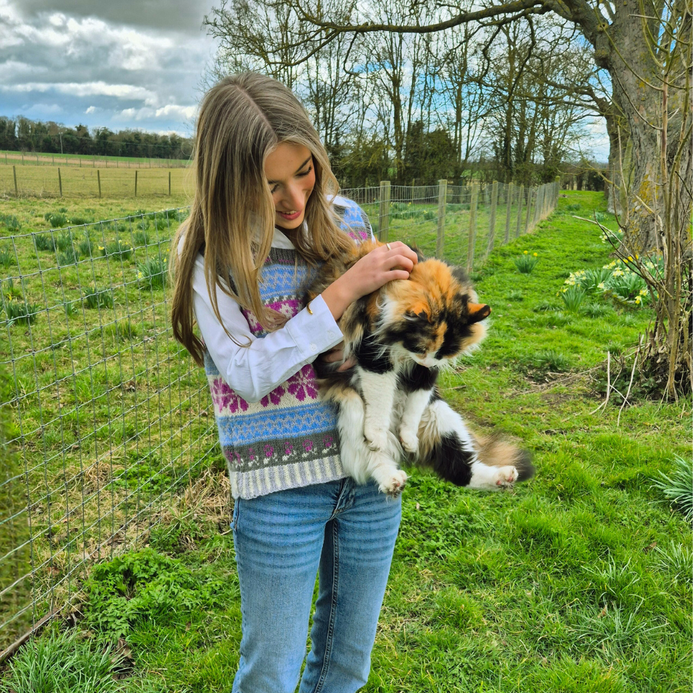 Woman holding a cat in a field with trees and a fence in the background