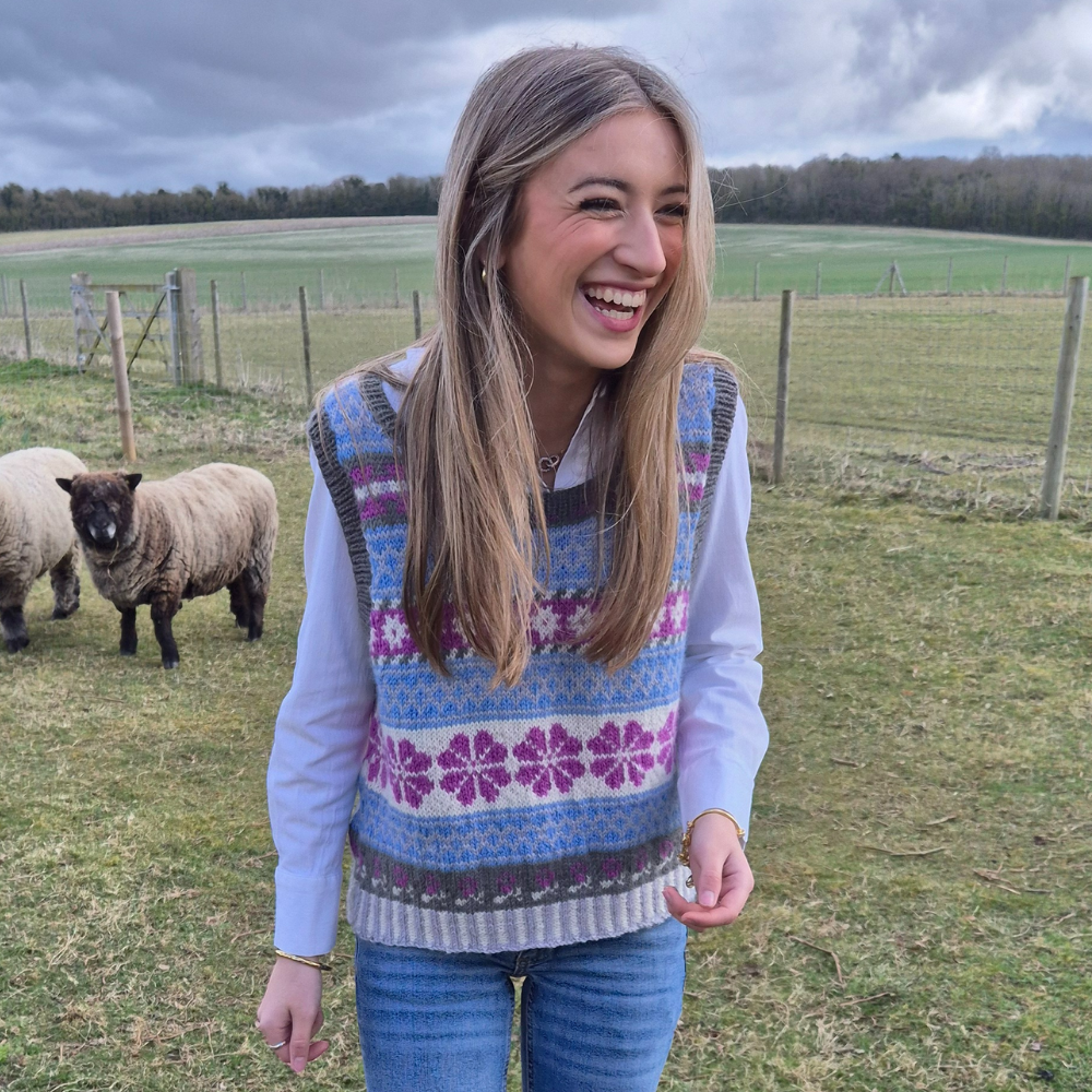 Woman wearing a patterned sweater vest standing in a field with sheep