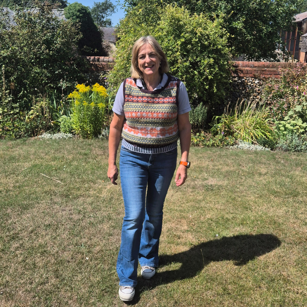 Woman standing in a garden wearing a patterned sleeveless top and blue jeans.