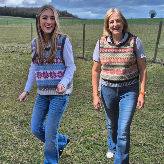 Two women walking outdoors in a field wearing Fair Isle vests.